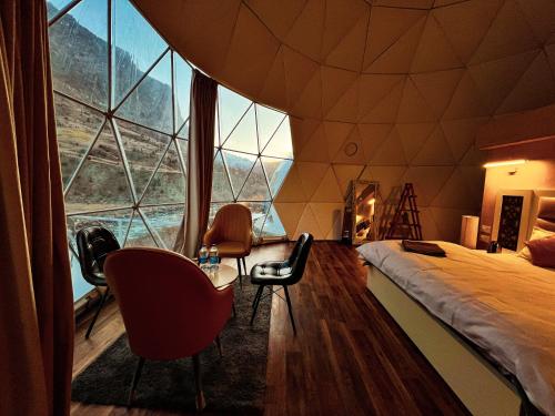 een kamer met een bed en stoelen en een groot raam bij YOLO Outdoors - Riverside Luxury Domes, Jispa in Jispa