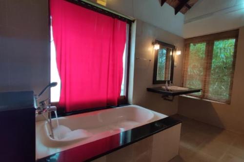 a bathroom with a large tub with a pink shower curtain at Rain Clouds Wayanad Forest Retreat - The Best Couple Friendly Private Cottages with Bathtub in Wayanad
