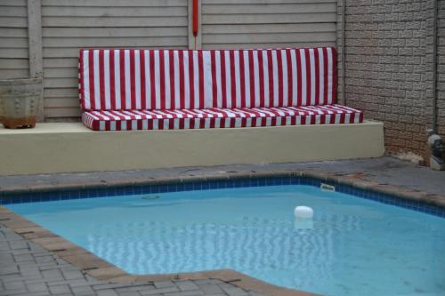 um banco vermelho e branco sentado ao lado de uma piscina em Durban Italian villa 1&2 em Durban