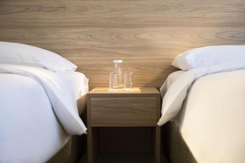 two beds with white sheets and two glasses on a night stand at Continental Hotel Lausanne in Lausanne