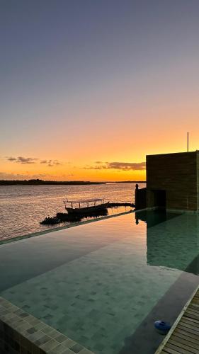 a swimming pool with a sunset over the water at Vila Piá in Piaçabuçu