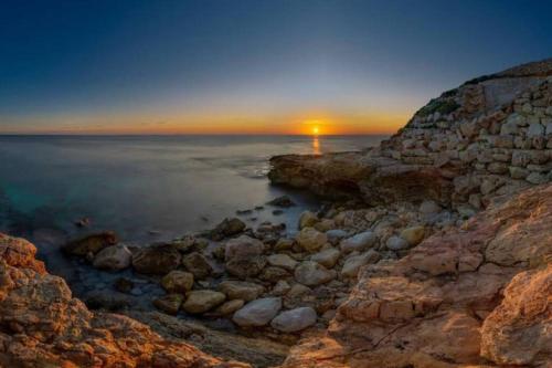 a sunset over the ocean with rocks on the shore at SeaWaves Apartments in Xgħajra