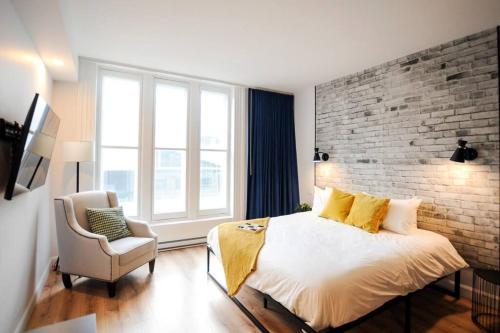 een slaapkamer met een bakstenen muur en een bed en een stoel bij The Old Fashioned Downtown Qc in Québec