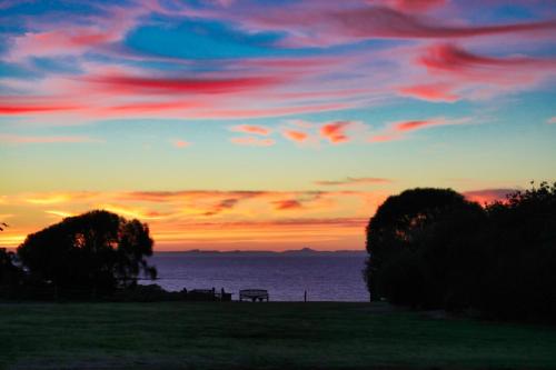 a sunset over the water with a bench in a field at Bear Gully Coastal Cottages in Walkerville