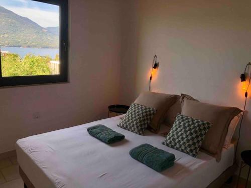 um quarto com uma cama com almofadas e uma janela em Charmante petite maison magnifique vue mer em Propriano