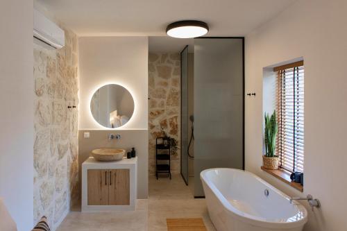 y baño con bañera, lavabo y espejo. en Casa Prasoul Villa with Heated Pool & Fitness area, en Prasiaí