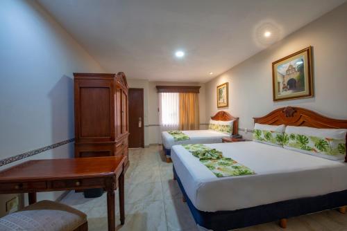 a bedroom with two beds and a table and a desk at Hotel del Gobernador in Mérida