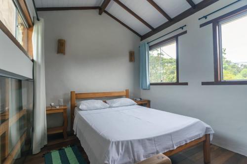 a bedroom with a white bed and two windows at Vila Guaiamum in Cumuruxatiba