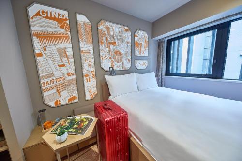 a room with a bed and a table with a red suitcase at lyf Ginza Tokyo in Tokyo