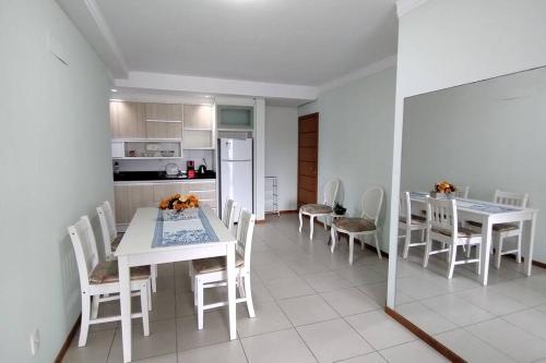 uma cozinha e sala de jantar com mesas e cadeiras brancas em Apartamento 2 quartos na praia em Florianópolis