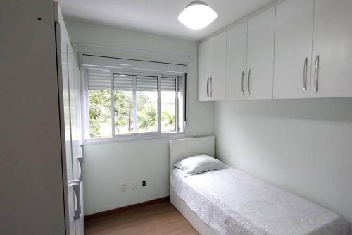 um quarto branco com uma cama e uma janela em Apartamento 2 quartos na praia em Florianópolis