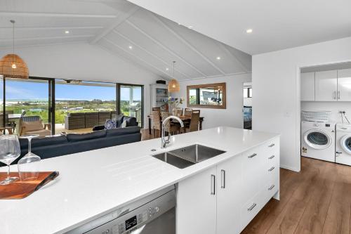 a white kitchen with a sink and a living room at Seaglass - Karikari Peninsula Holiday Home in Kaitaia