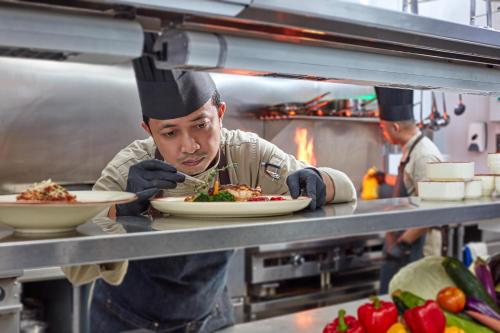 a chef preparing a plate of food in a kitchen at Mardhiyyah Hotel and Suites in Shah Alam