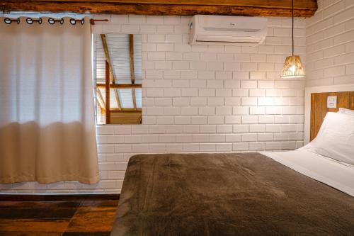 a bedroom with a bed and a white brick wall at Pousada Hanalie in Praia do Rosa