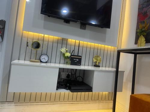 a shelf with a tv and a clock on a wall at AMERICANA LUXURY APARTMENT in Lekki
