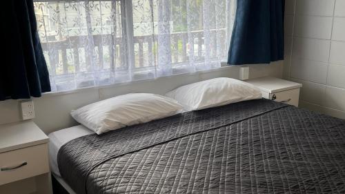 1 dormitorio con 1 cama con 2 almohadas y ventana en Aaron Court Motel Whangarei en Whangarei