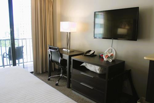 a hotel room with a desk with a television and a bed at Elevated Aqua Palms Waikiki Studio condo in Honolulu