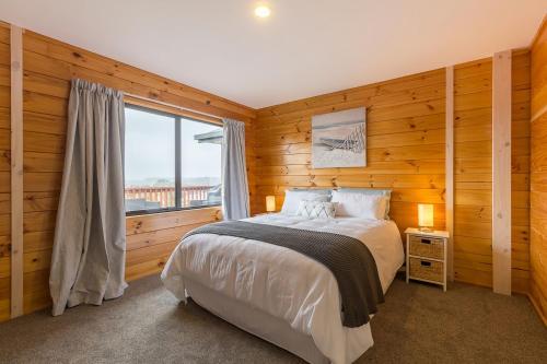 Sea Breeze في Mapua: غرفة نوم بجدران خشبية وسرير مع نافذة