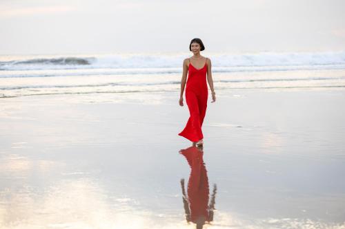 a woman in a red dress walking on the beach at Grand Mercure Bali Seminyak in Seminyak