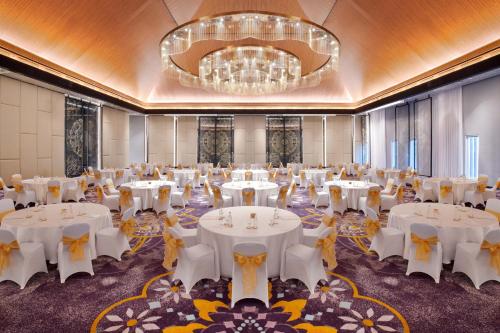 a ballroom with white tables and chairs and a chandelier at Grand Mercure Bali Seminyak in Seminyak