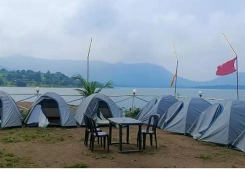 a group of tents and a table and chairs in front of the water at Pawna lake Camping Lonavala in Kolvan