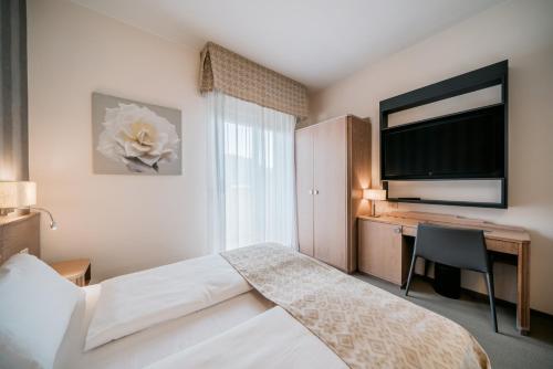 a bedroom with a bed and a desk with a television at Hotel Europa Lignano in Lignano Sabbiadoro