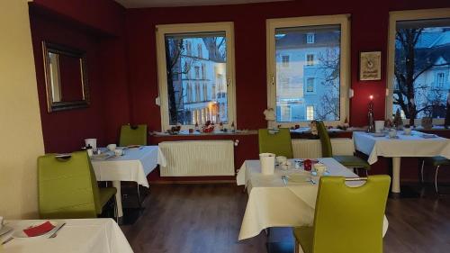 um restaurante com mesas brancas, cadeiras verdes e janelas em Ricks City Hotel em Trier