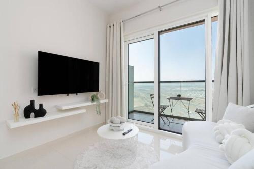 a white living room with a television and a white couch at Crème De La Cozy 1 Bedroom in Dubai