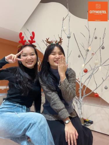 two women sitting next to each other in front of a christmas tree at City Hostel Da Nang in Da Nang