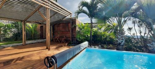 una piscina en una terraza de madera junto a una casa en Bungalow cosy avec piscine surplombant l'océan, en Bellemène
