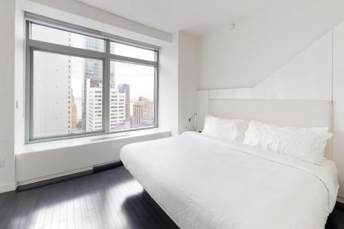 a white bedroom with a large white bed and a window at Financial District 1br w WD gym elevator NYC-1369 in New York