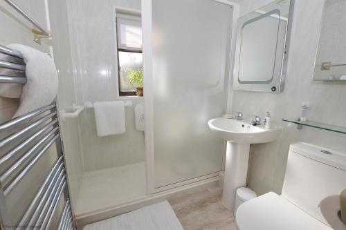 a white bathroom with a sink and a shower at The Den in Sheringham