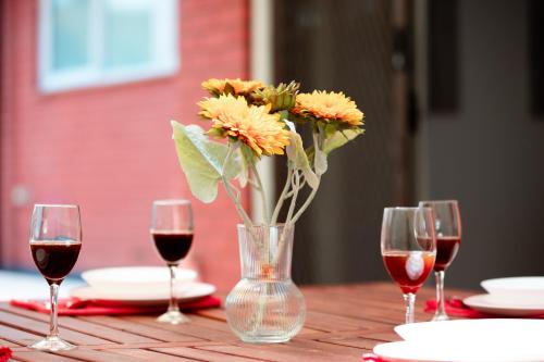 a vase with flowers sitting on a table with wine glasses at Modern Cozy Retreat-4Bedroom, Full Kitchen, Coffee Machine, Cot, Pets allowed-Fully Fenced,FreeWifi, Netflix, 2TV in Campbelltown