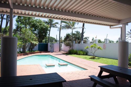 a swimming pool with a bench and a pergola at Palm Cove - 52 Chakas Cove, Penthouse-Literally on the Beach in Ballito
