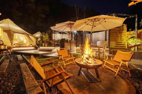a fire pit with chairs and umbrellas on a patio at fabula glamping in Kimitsu
