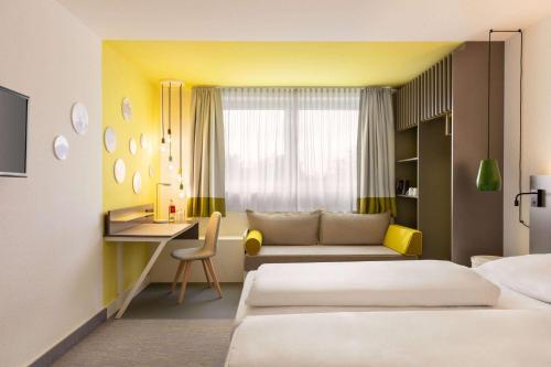 a hotel room with a bed and a desk and a couch at Vienna House Easy by Wyndham Neckarsulm in Neckarsulm