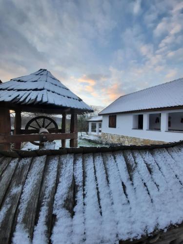 a snow covered wooden table with a wheel and a house at Acul în carul cu fan in Pădurenii