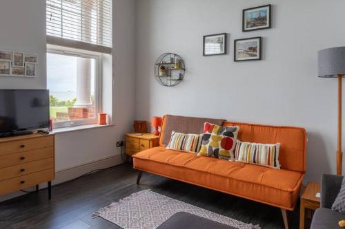 an orange couch in a living room with a window at Waves@Walpole - 2 Bed Flat with Amazing Sea Views in Margate