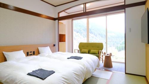 a bedroom with a large white bed and a green chair at Miharashinoyado Fronden in Hita