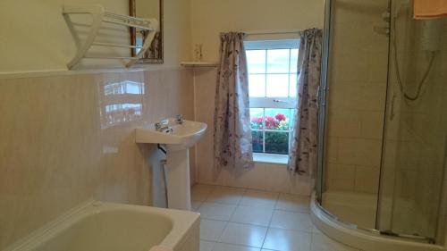 uma casa de banho com um lavatório, um chuveiro e uma janela. em John Morgans House em Portmagee