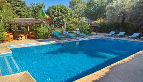 uma piscina com cadeiras azuis e um gazebo em Auberge Plein Soleil em Mbodiène