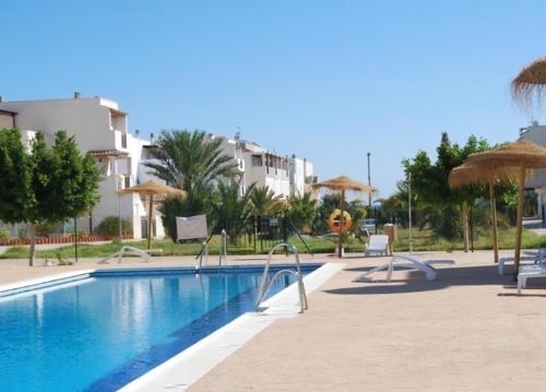 a swimming pool with chairs and umbrellas next to a building at APARTAMENTO URBANIZACION 1ºLINEA DE PLAYA NUDISTA in Vera