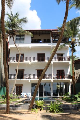 a white building with palm trees in front of it at PRANA Beach Hotel Hikkaduwa in Hikkaduwa