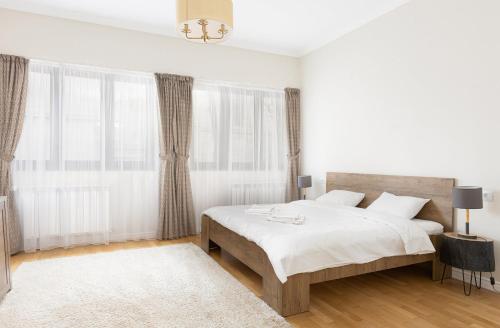 a white bedroom with a large bed and windows at Cranta Hillside Apartment in Braşov