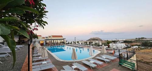 une grande piscine avec des chaises longues blanches dans l'établissement LINDOS HORIZON, à Lindos