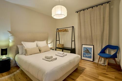 - une chambre avec un grand lit blanc et une chaise bleue dans l'établissement Appart' Jeannette en Hyper centre ville avec balcon et Parking sous-terrain, by PRIMO C0NCIERGERIE, à Nevers