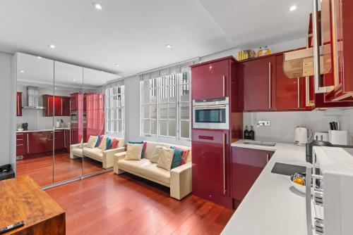 uma cozinha com armários vermelhos e sofás num quarto em Londwell, Sloane Square Gem, Private Terrace Suite em Londres