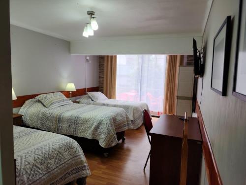 a room with three beds and a table and a window at NEW HOTEL CRUZ DEL SUR in Concepción