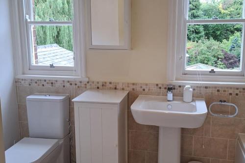 a bathroom with a sink and a toilet and two windows at Stunning 3BD Victorian House in Bramhall Village in Bramhall