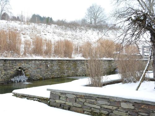 a stone wall in the snow next to a river at Charming house with fireplace in Bièvre